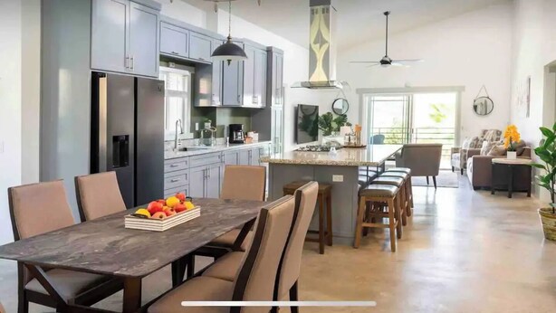 Una cocina moderna con gabinetes grises, una isla central y un comedor con mesa y sillas de madera.