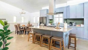Una cocina moderna con una isla central, taburetes de bar y un comedor con sillas.