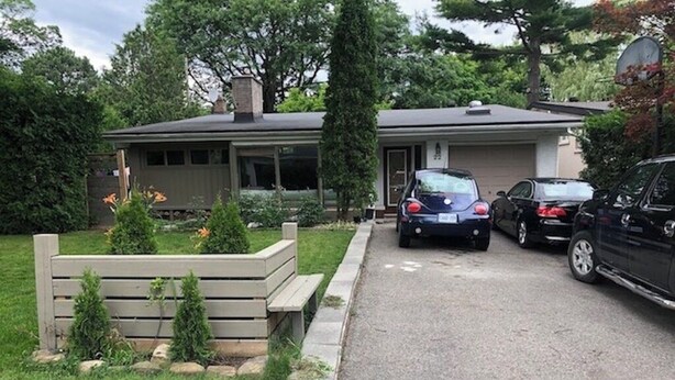A residential driveway with two cars parked, a house with a dark roof, and a well-maintained lawn with small shrubs.
