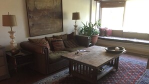 A cozy living room with a sofa, a coffee table, a lamp, a potted plant, and a window with a view.