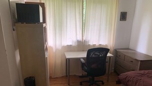 A bedroom with a bed, a desk, a chair, a radiator, and a window with curtains.