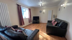 A living room with two black leather sofas, a flat-screen TV, wooden flooring, and a ceiling fan. - Spacious Home from Home! Perfect for Farnborough Airshow.  (Farnborough)