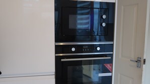 A compact kitchen with a built-in oven and microwave, white cabinetry, and a door leading to another room. - Spacious Home from Home! Perfect for Farnborough Airshow.  (Farnborough)