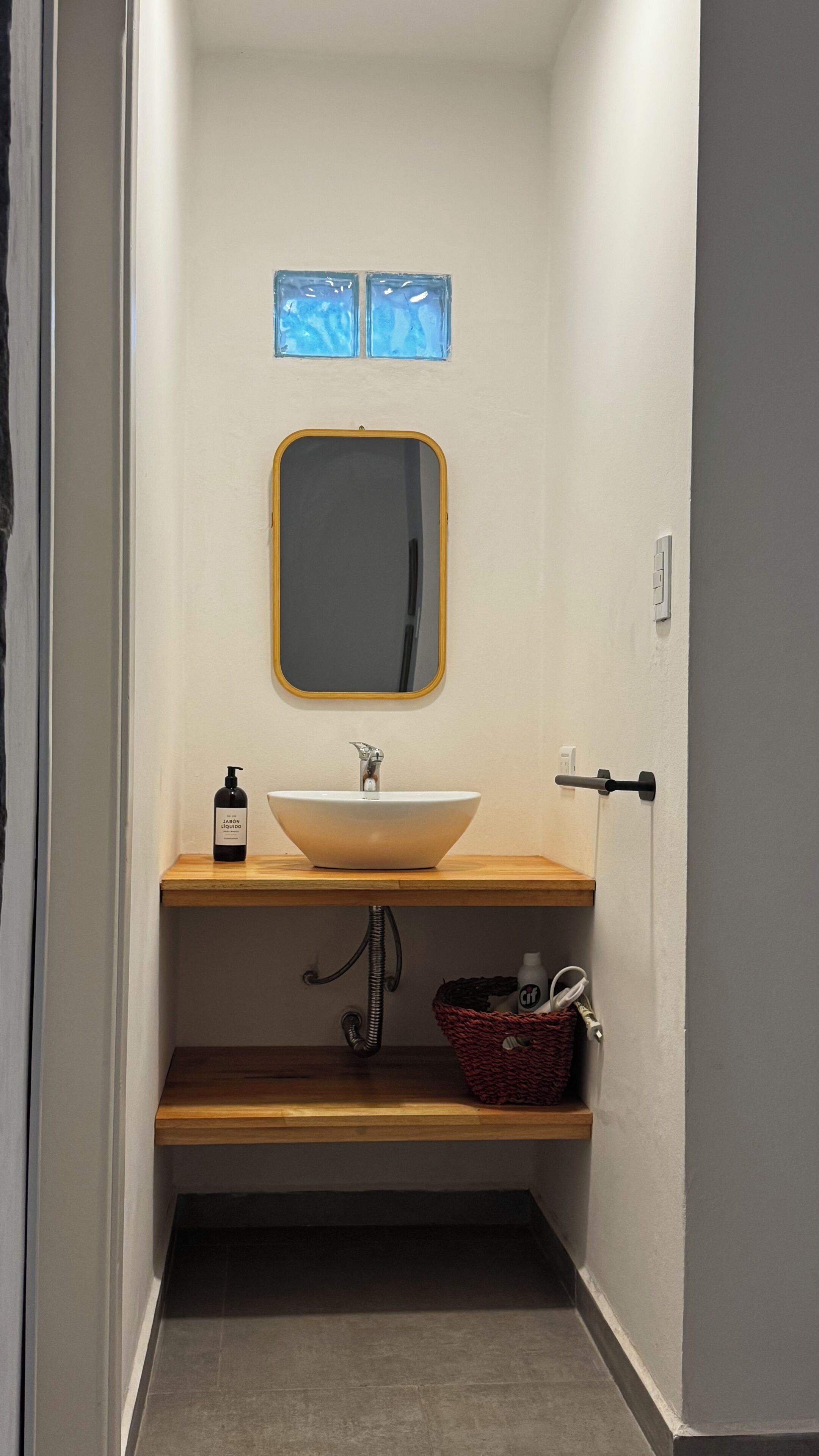 Une salle de bain avec un lavabo blanc, un miroir, un flacon de savon liquide, un panier et un porte-serviettes.
