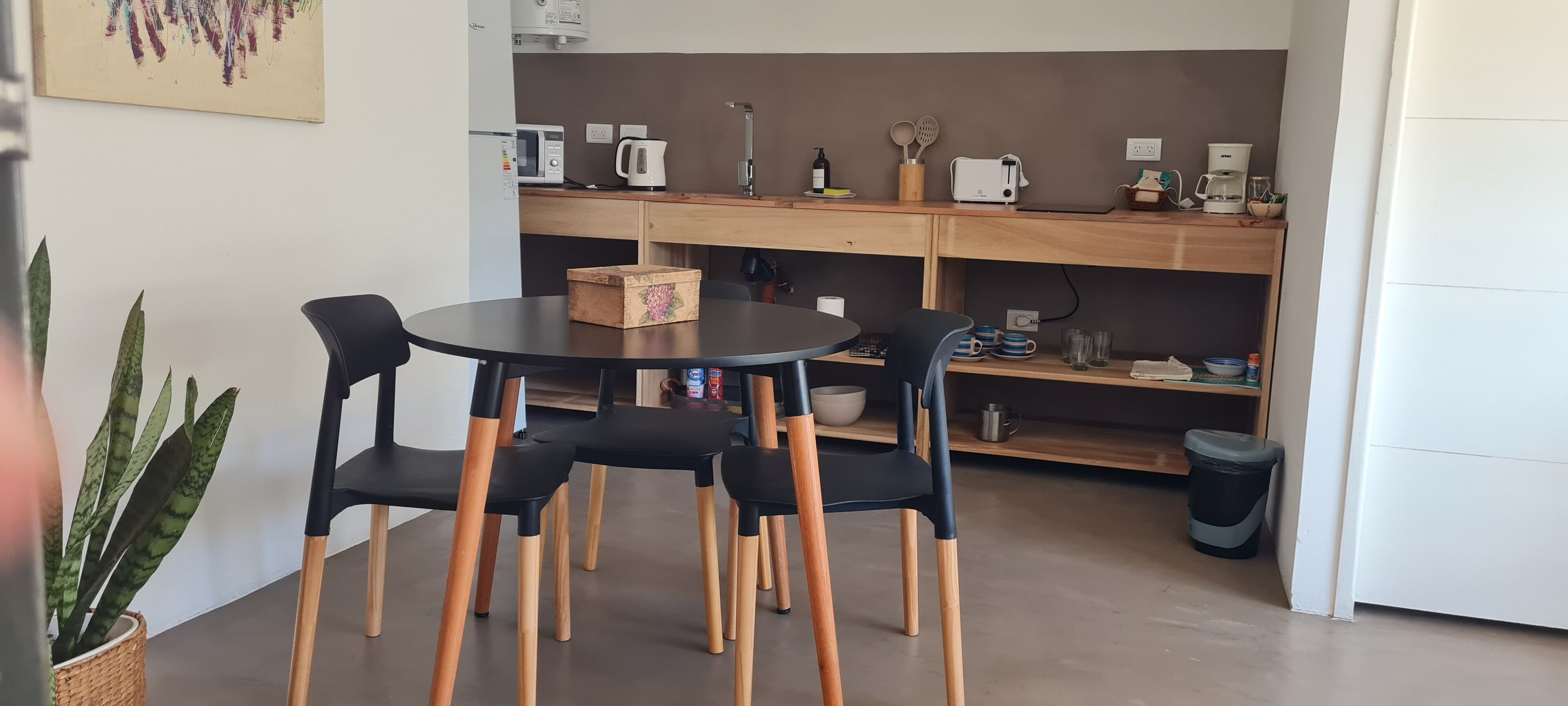 Una cuina compacta amb una taula rodona i quatre cadires, microones, cafetera i diversos utensilis de cuina damunt el taulell.