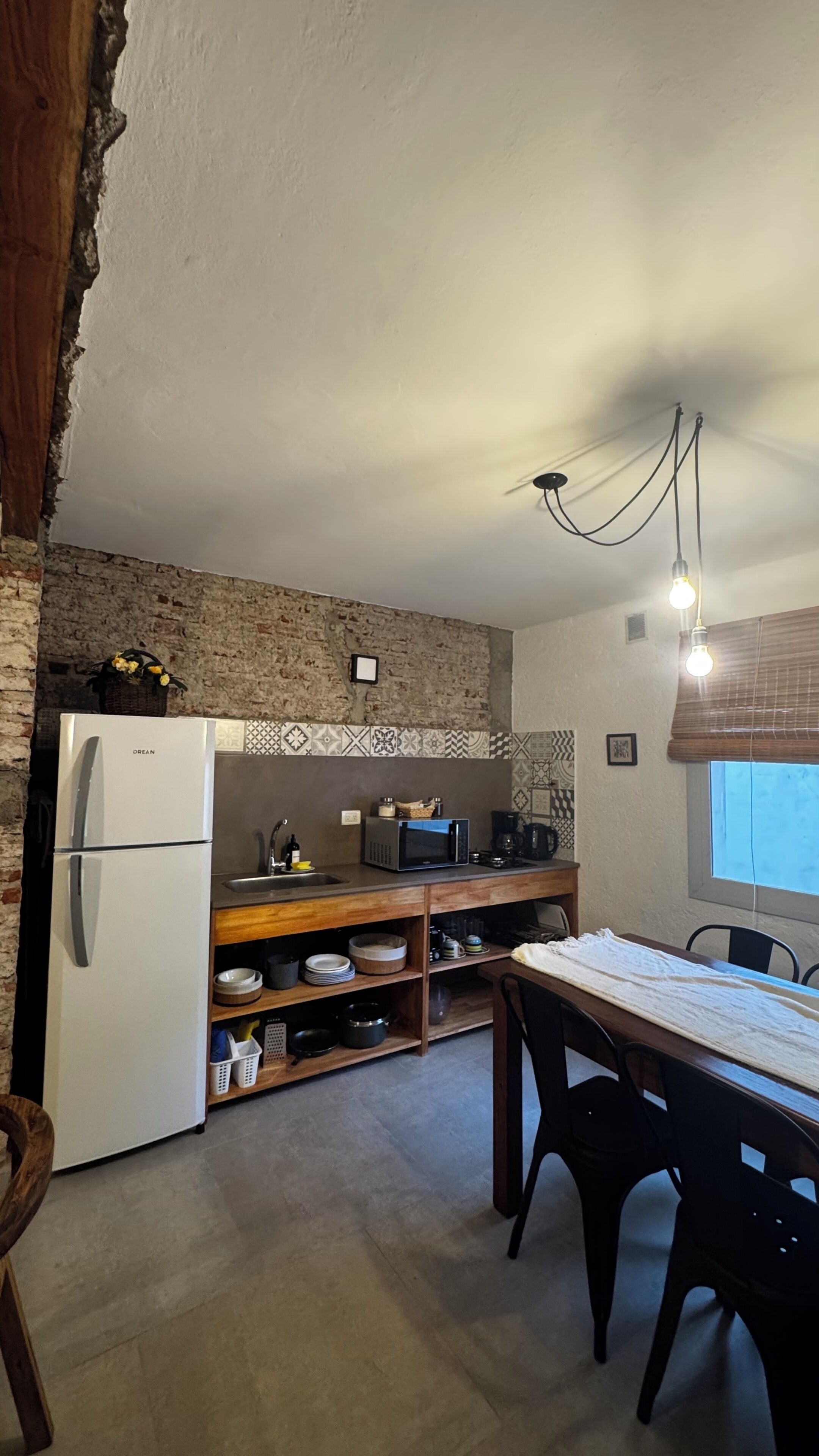 Cozinha compacta com geladeira, micro-ondas e prateleiras de madeira.