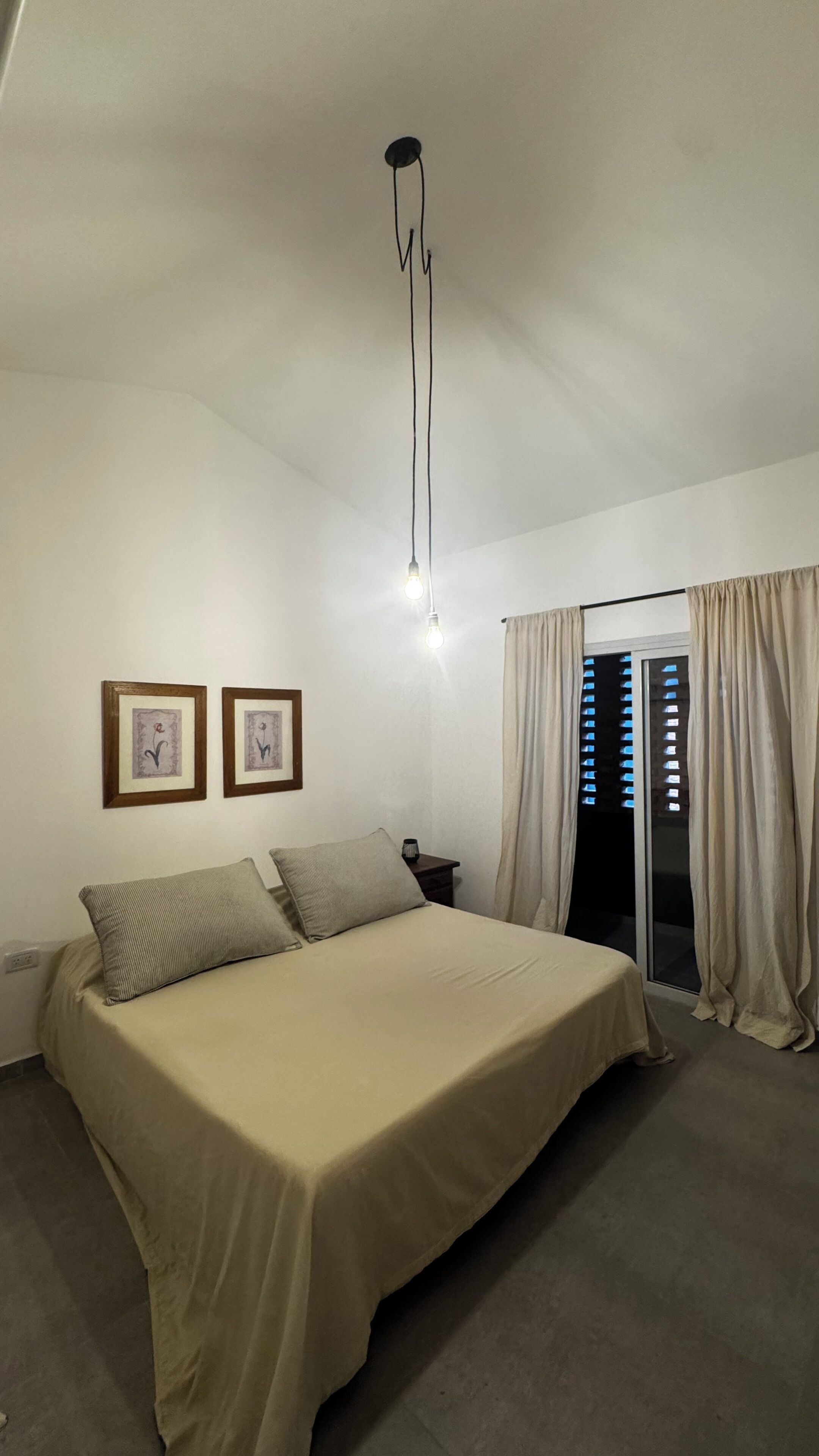 A bedroom with a bed, two framed pictures, a nightstand, a lamp, and a window with curtains.
