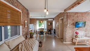 Amplia sala de estar con pared de ladrillo, una mesa de comedor y un televisor montado en la pared.