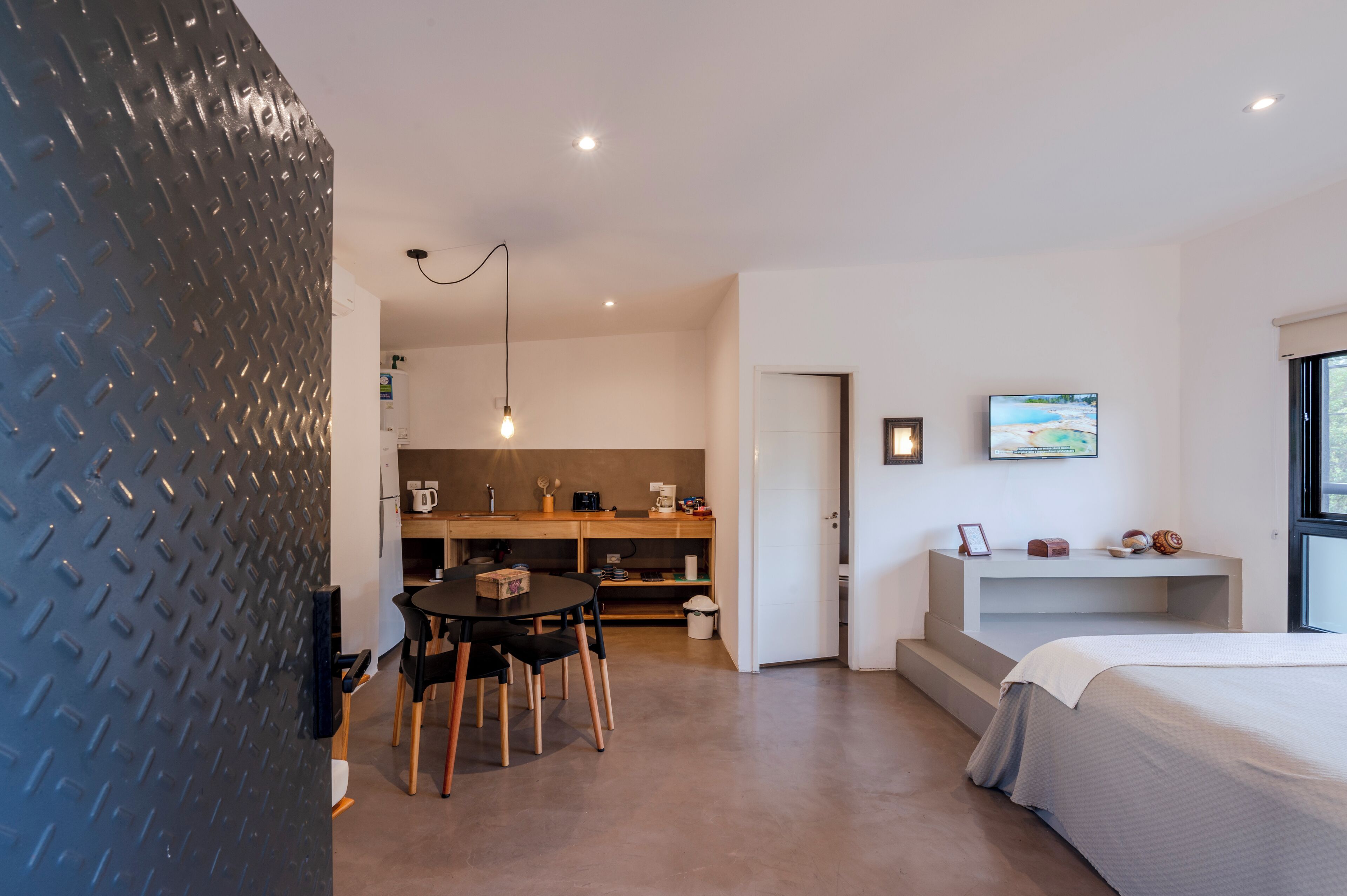 A modern hotel room with a dining area, kitchenette, and a large bed.