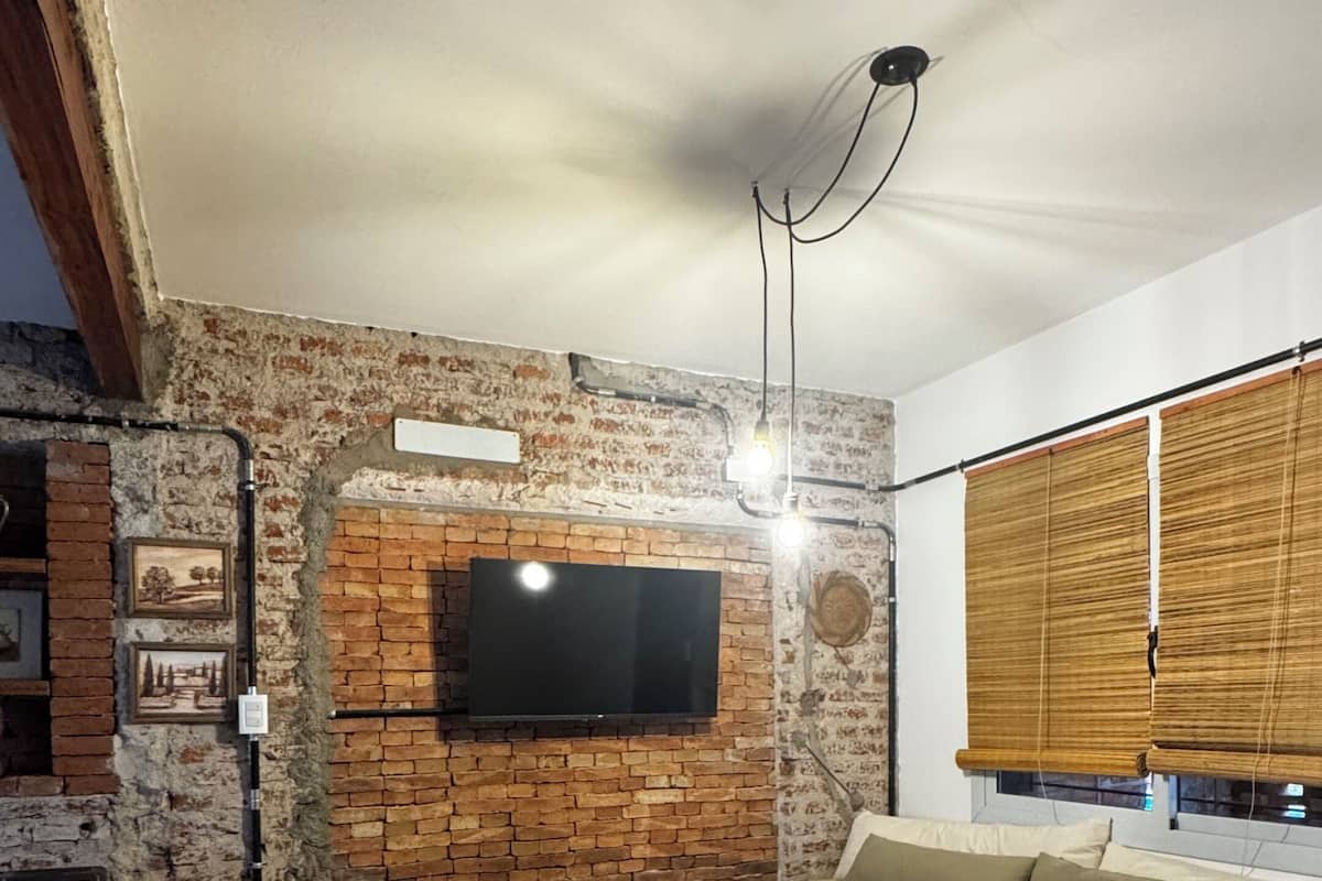 Ett vardagsrum med en tegelvägg, en platt-TV, ett soffbord i trä, en soffa och ett fönster med persienner.