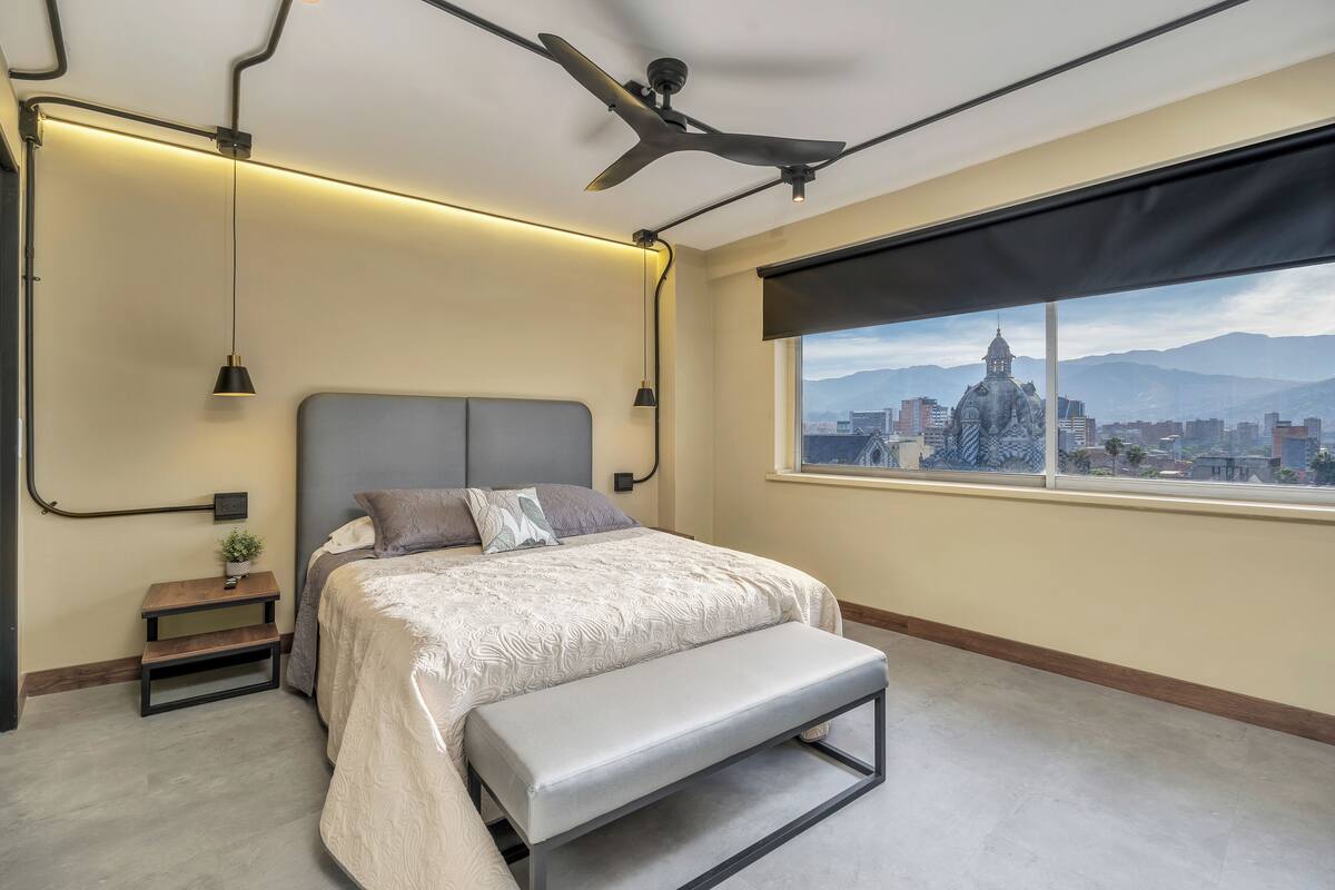 Een moderne slaapkamer met een bed, bankje, nachtkastje en uitzicht over de stad.