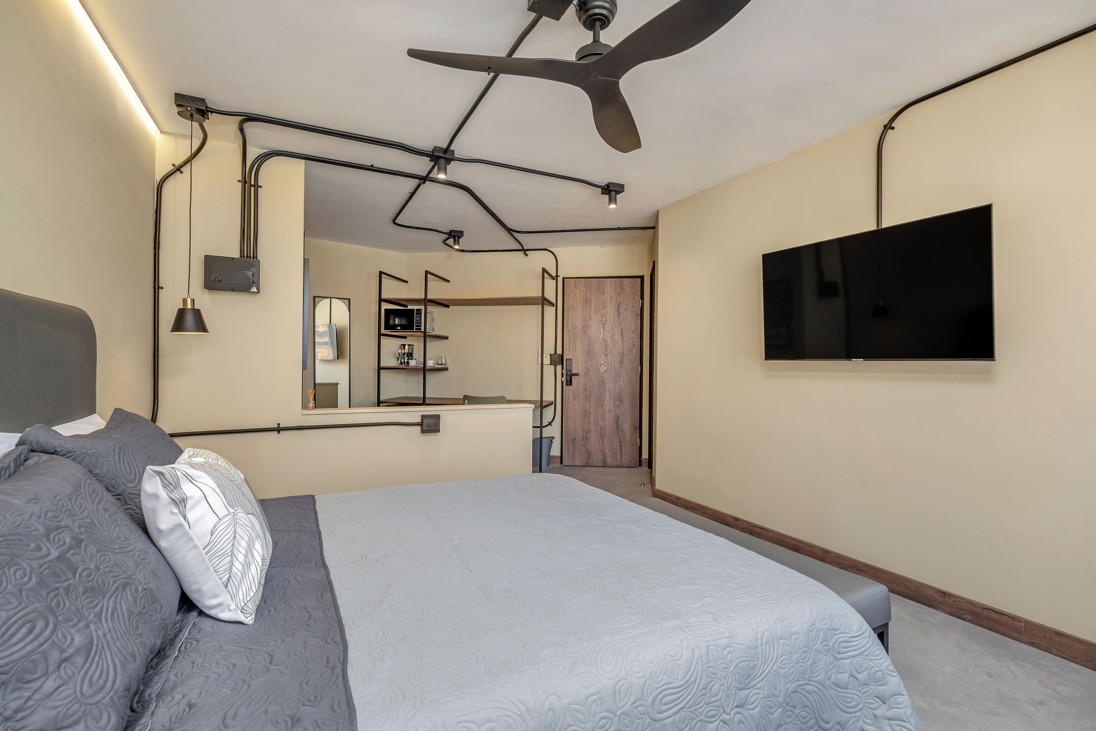 A modern bedroom with a bed, a ceiling fan, a TV, and a bathroom visible through an open door.