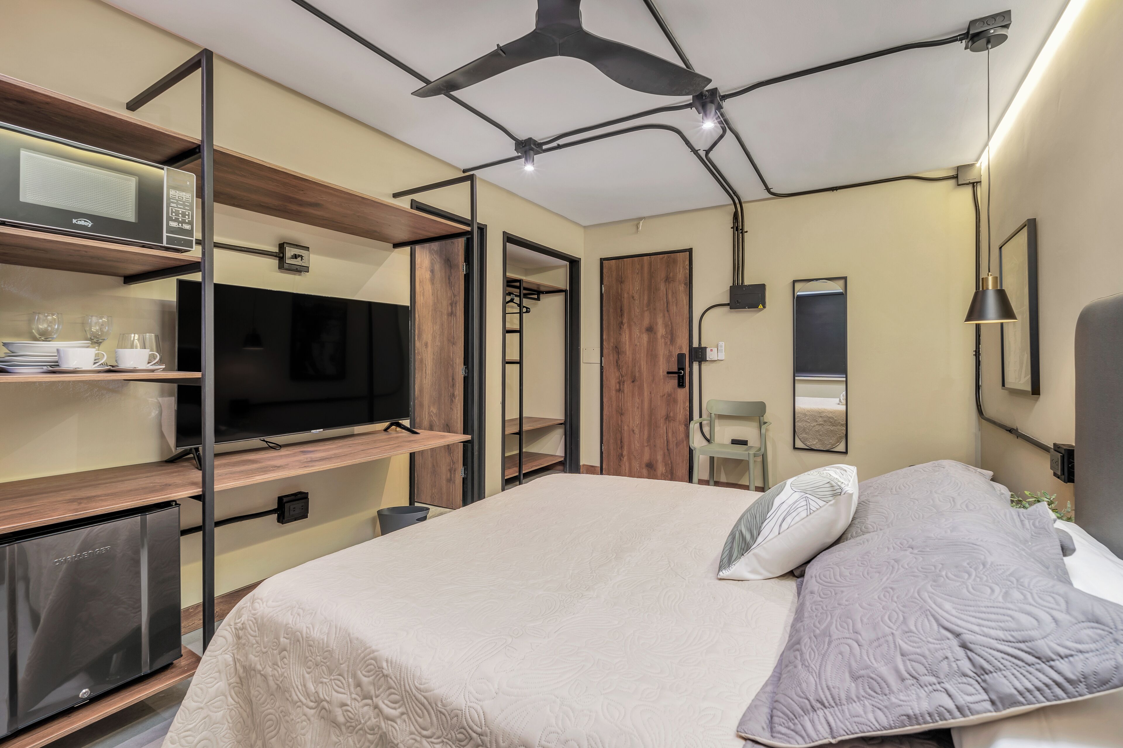 A modern bedroom with a bed, a TV, a mini-fridge, and a wardrobe.