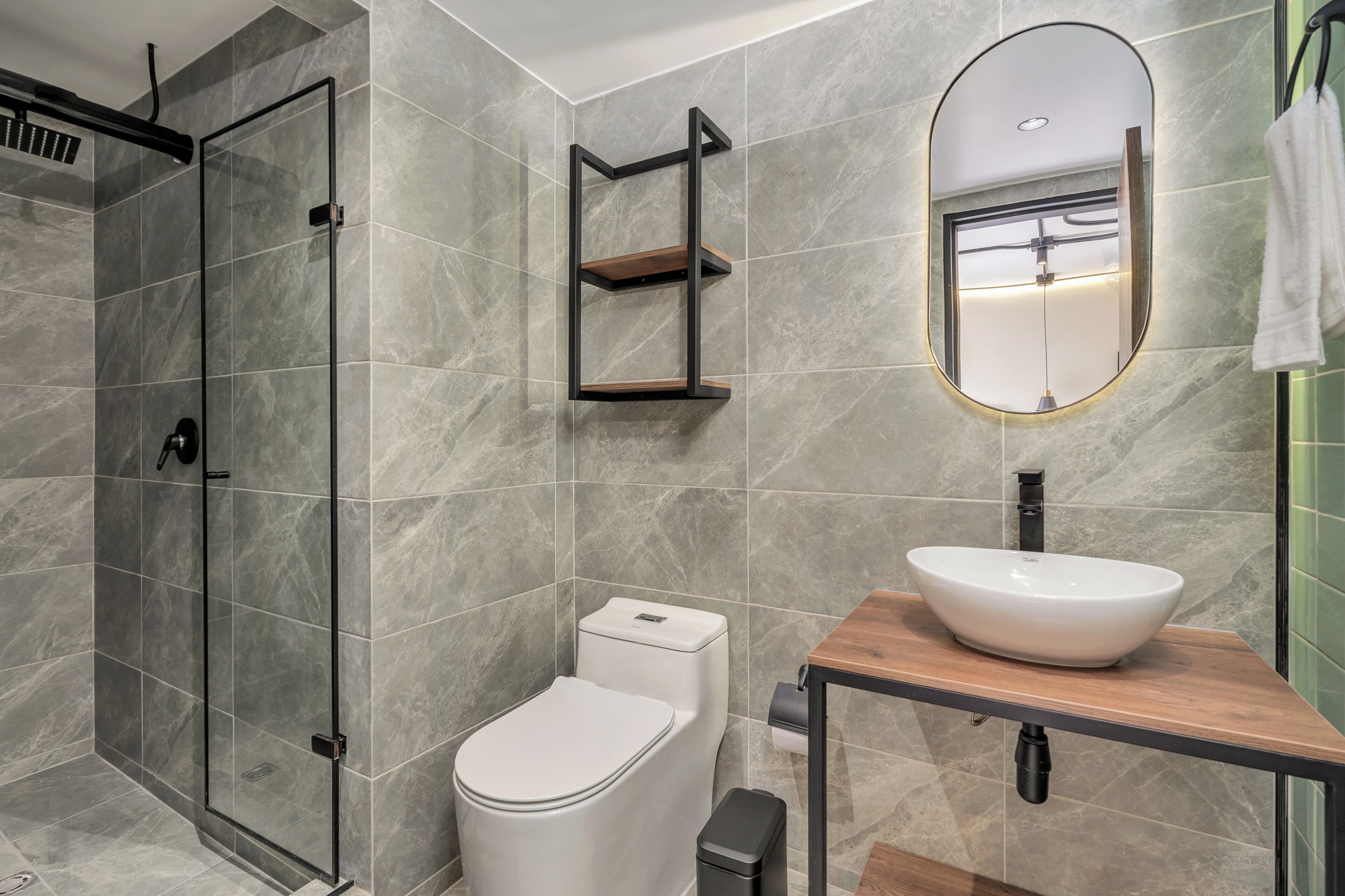 A modern bathroom with a glass shower enclosure, a toilet, a sink with a wooden countertop, and a mirror with a gold frame.