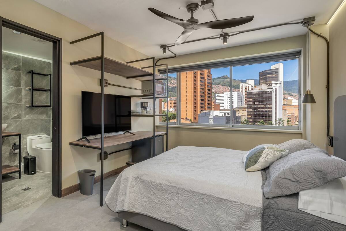 Een moderne slaapkamer met een bed, televisie en uitzicht op de stad.