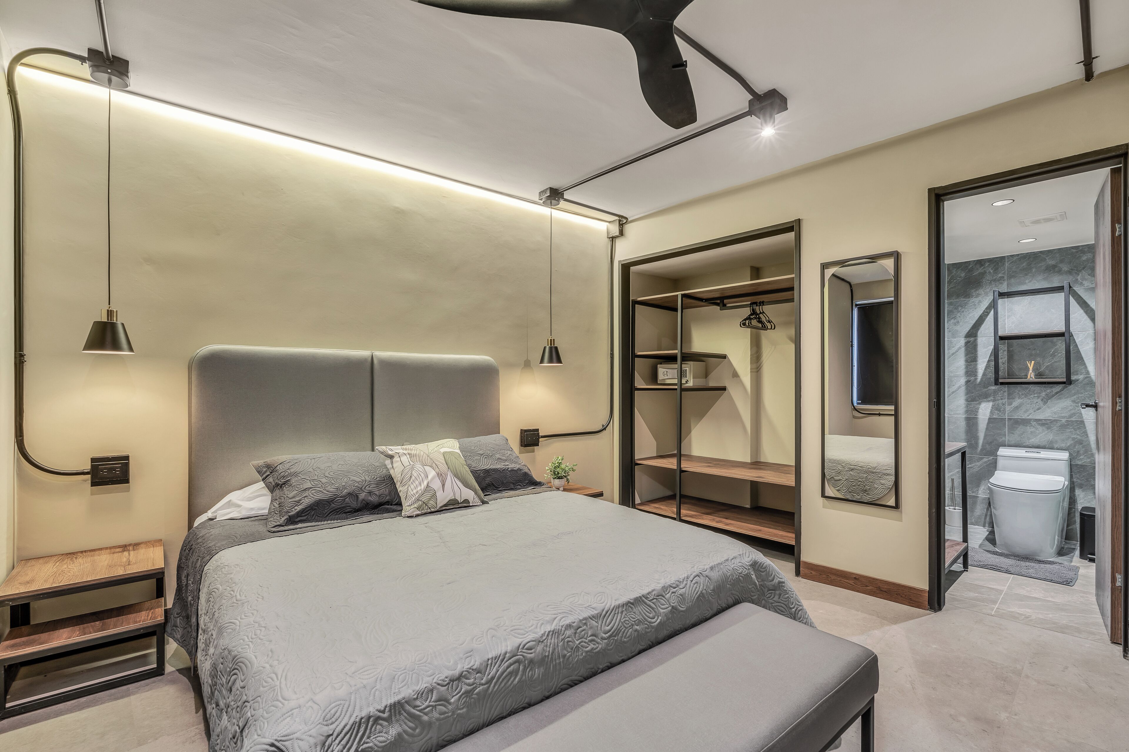 Un dormitorio moderno con una cama grande, mesitas de noche, un banco y un vestidor con espejo y estanterías.