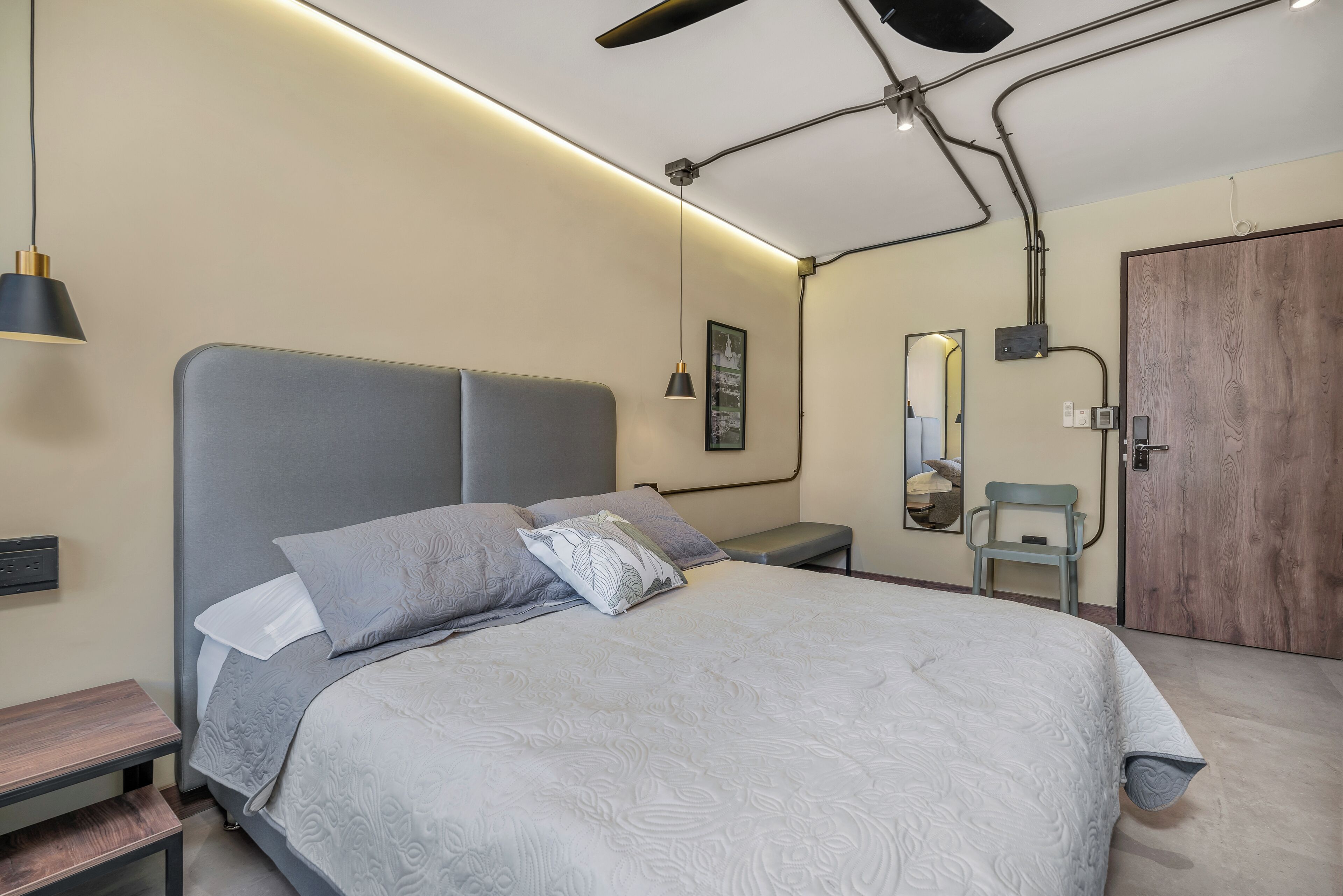 Un dormitorio moderno con una cama grande, mesitas de noche, un banco, un ventilador de techo y una puerta de madera.
