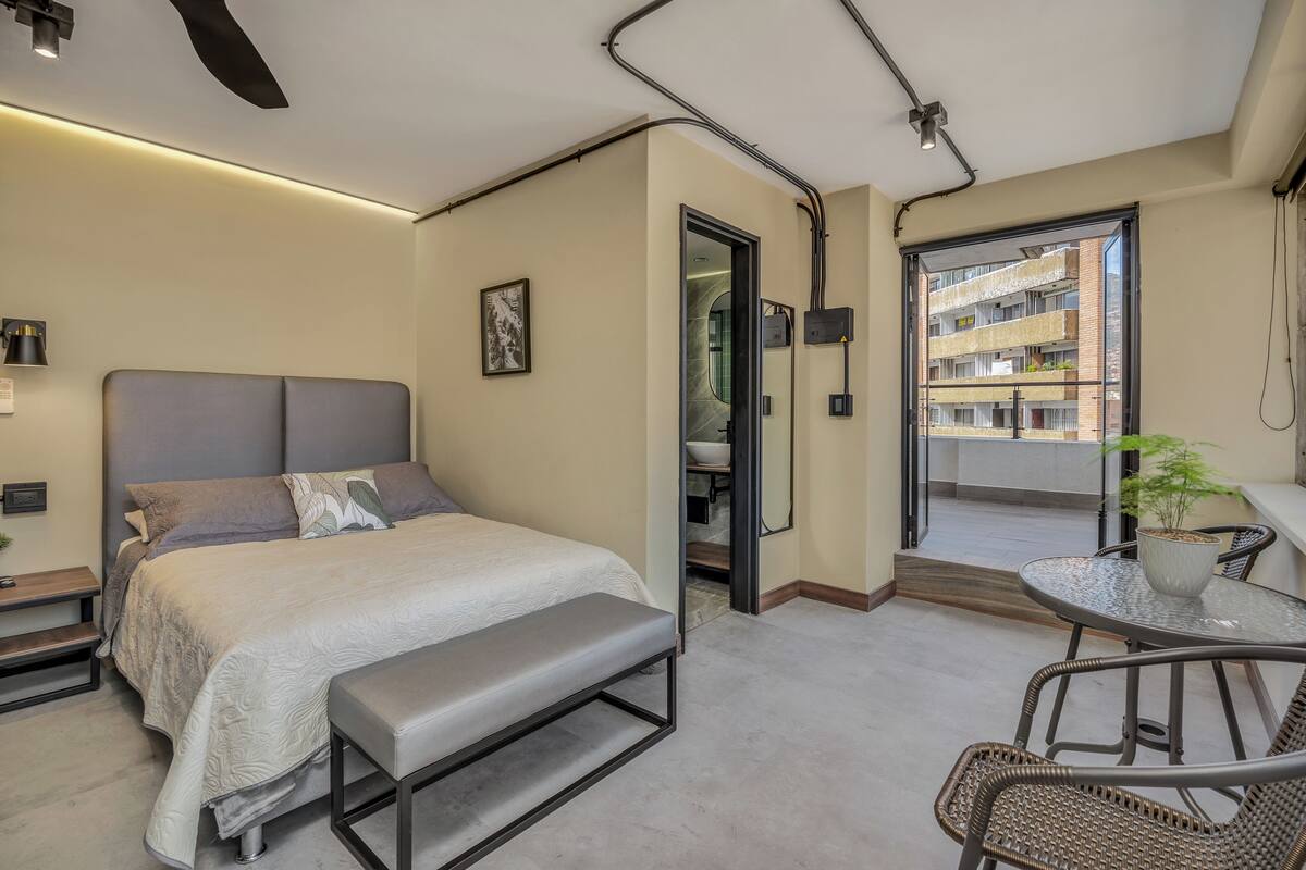 Een moderne slaapkamer met een bed, een bankje en een balkon met een tafel en stoelen.