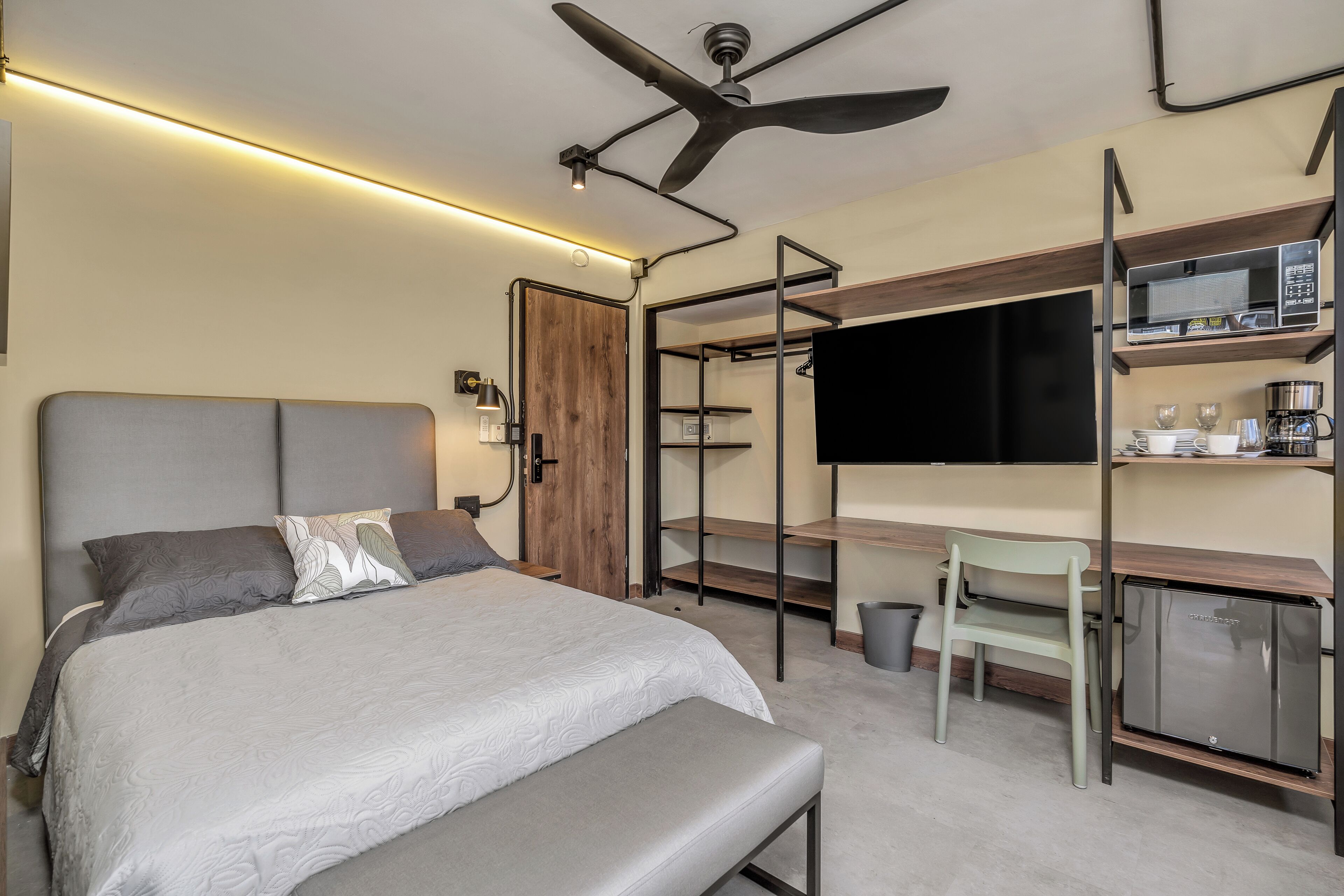 A modern bedroom with a bed, desk, chair, TV, and built-in appliances.