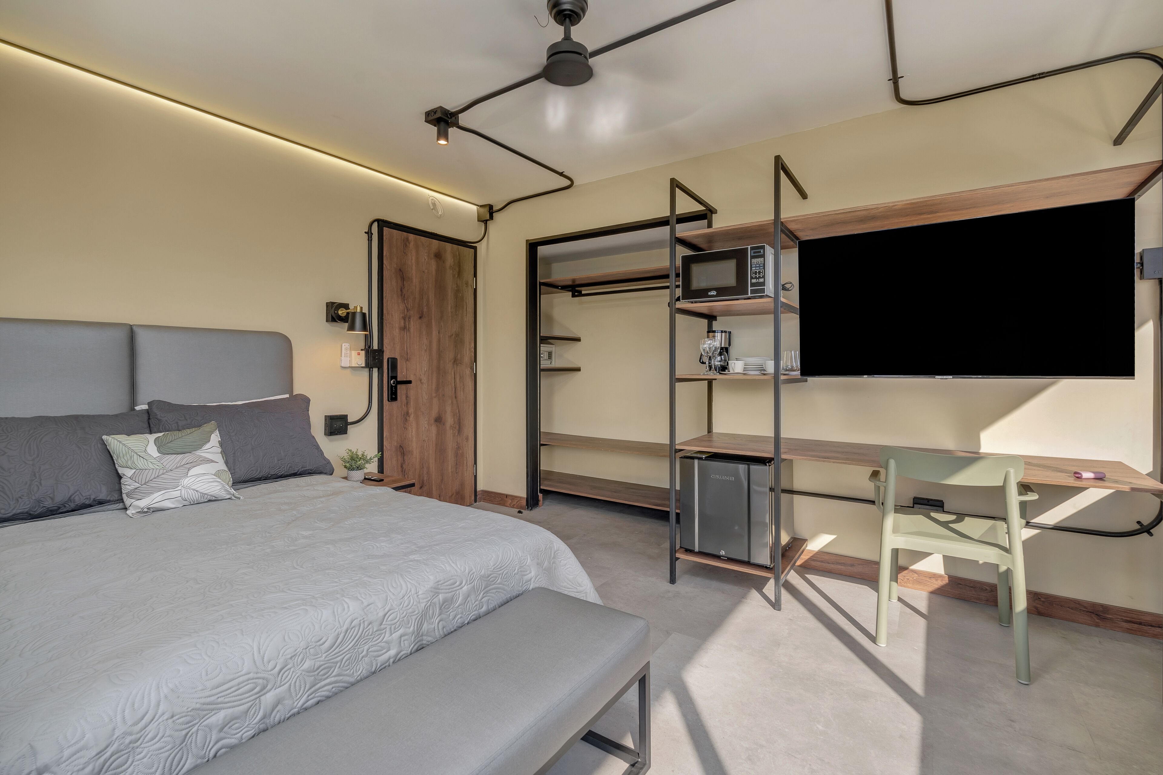 A modern bedroom with a bed, bedside table, desk, chair, and a TV.