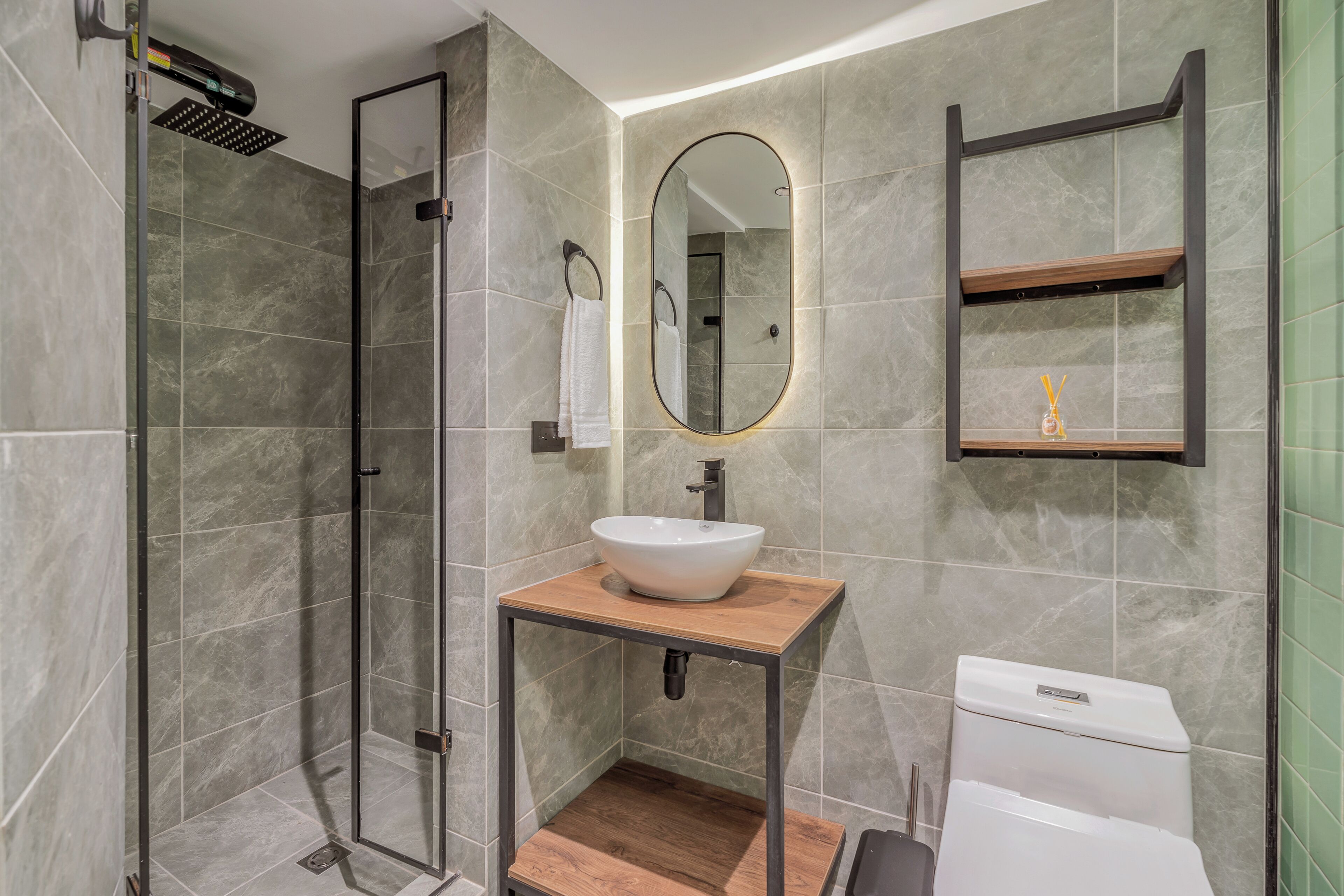 Un baño moderno con ducha envuelta en vidrio, tocador de madera con lavamanos blanco, espejo y retrete.