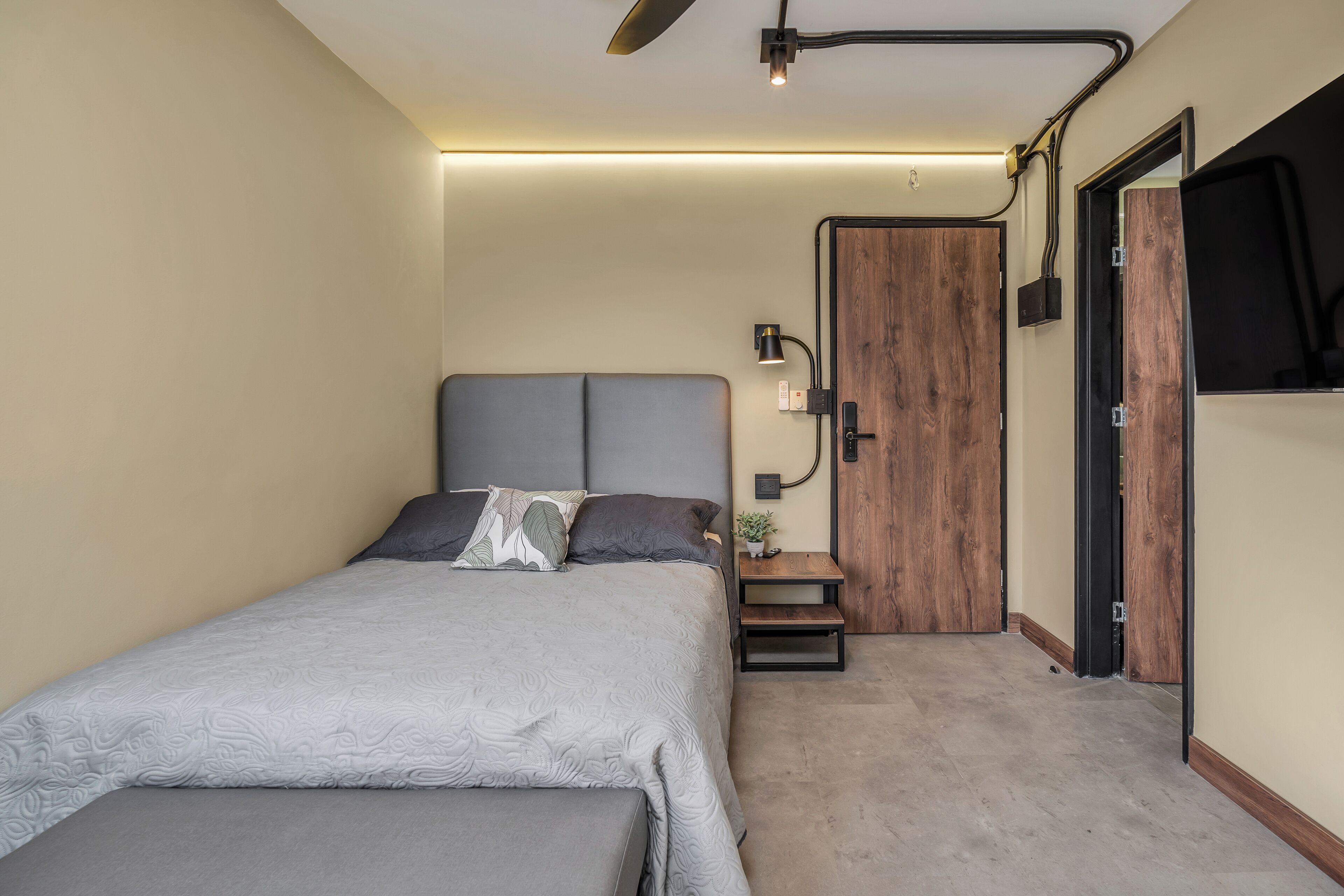 Un dormitorio moderno con una cama, mesitas de noche, un armario de madera y un televisor de pantalla plana montado en la pared.