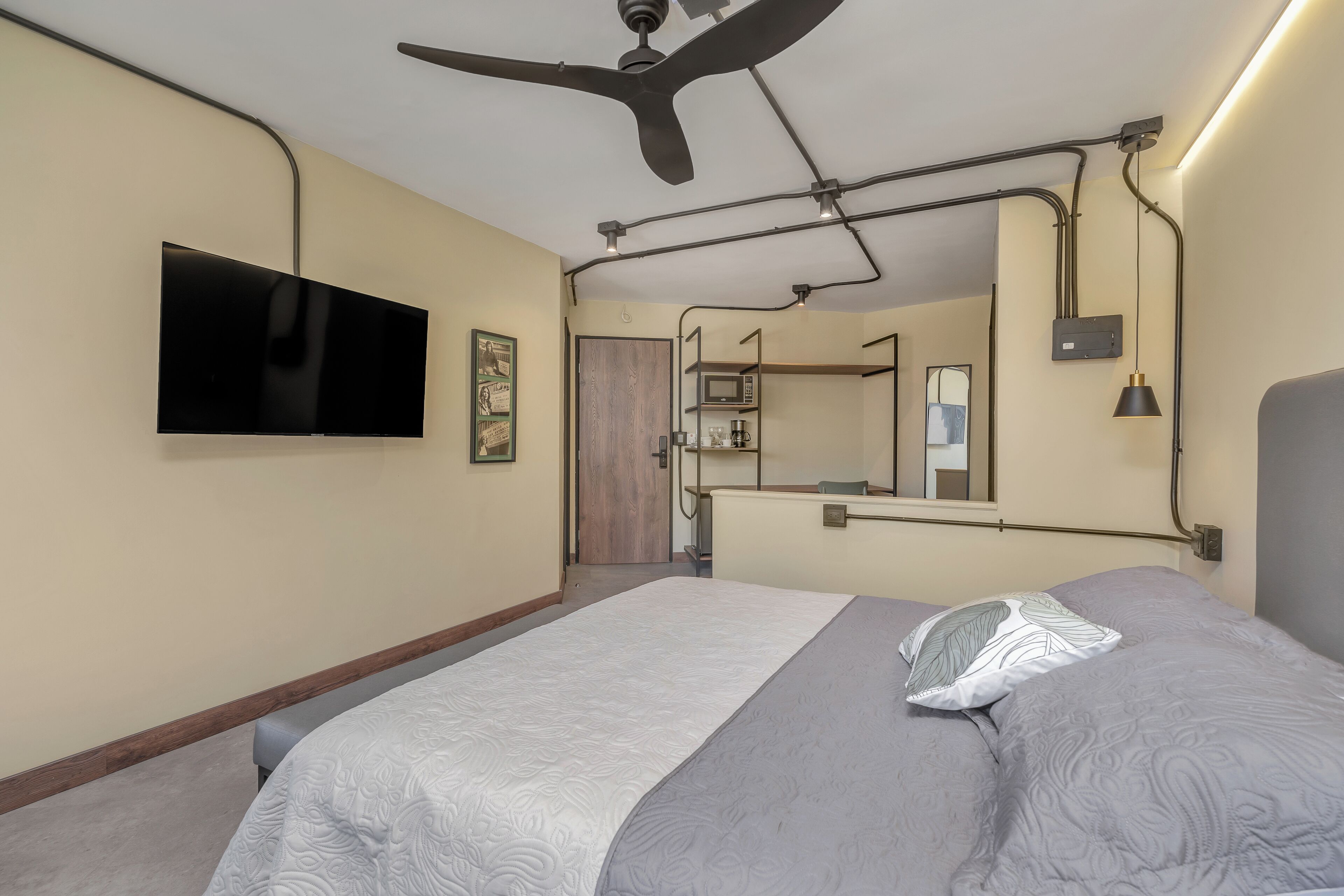 Habitació d'hotel moderna amb televisió de pantalla plana, ventilador de sostre i un llit gran amb roba de llit estampada.