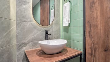 A bathroom with a wooden vanity, a white vessel sink, a mirror, and green tiled walls.