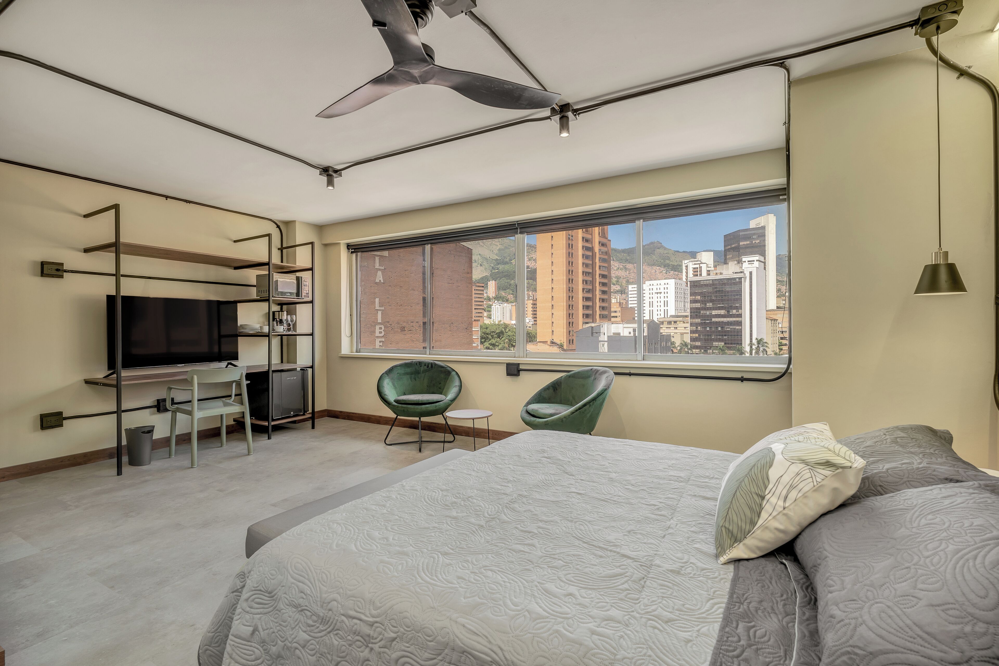 Una habitación de hotel moderna con una cama, un escritorio, un televisor y un amplio ventanal con vistas a la ciudad.