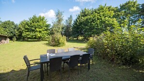 An outdoor dining area with a table and chairs, surrounded by greenery and trees.