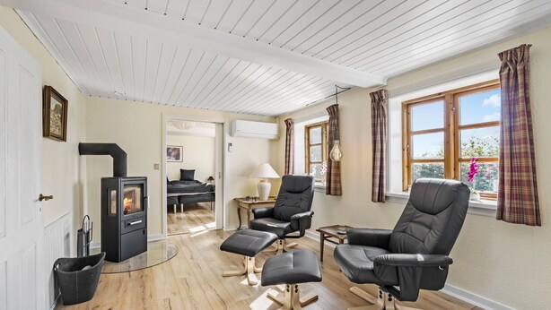 A cozy living room with a fireplace, leather chairs, wooden flooring, and large windows with curtains.