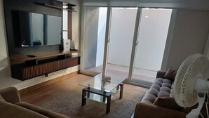Una sala de estar con una televisión de pantalla plana, una mesa de centro de vidrio, un sofá y un ventilador.