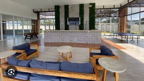 Un área de estar interior moderna con sofás, mesas y una pantalla de televisión.