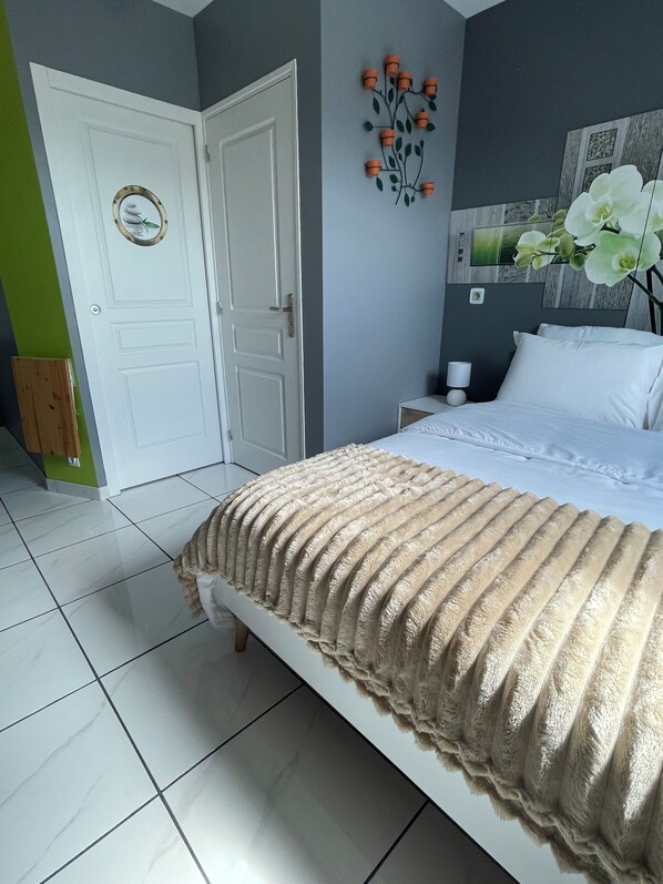 Un dormitorio con una cama, una mesita de noche, un reloj de pared y una planta decorativa.