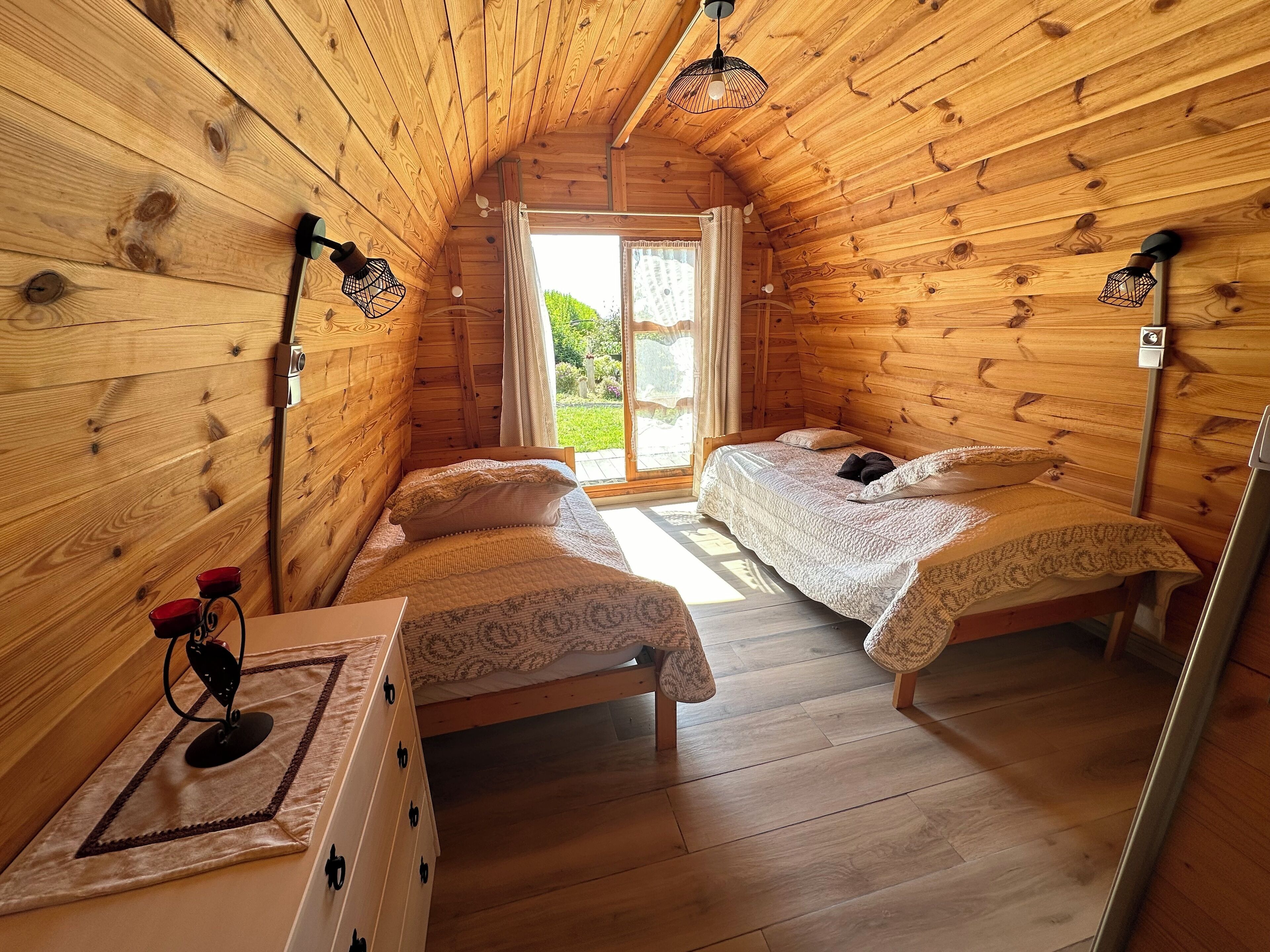 Un dormitorio acogedor de cabaña de madera, con dos camas, un tocador pequeño y una ventana con cortinas.
