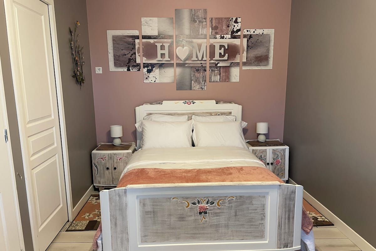 A bedroom with a bed, two bedside tables, a wall decoration with 'HOME', and a door.