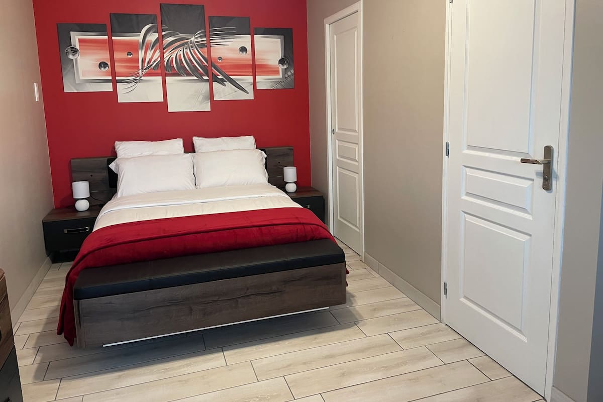 A bedroom with a bed, nightstands, a red wall, and a door.