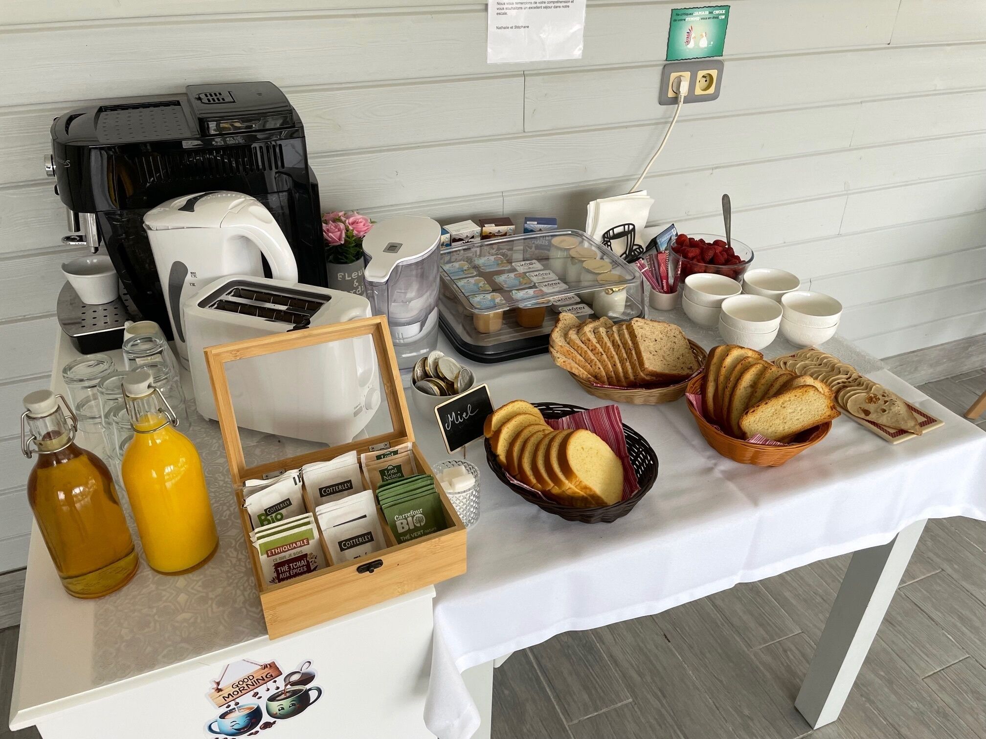 Una mesa de desayuno buffet con cafeteras, pan, bollería y salsas.