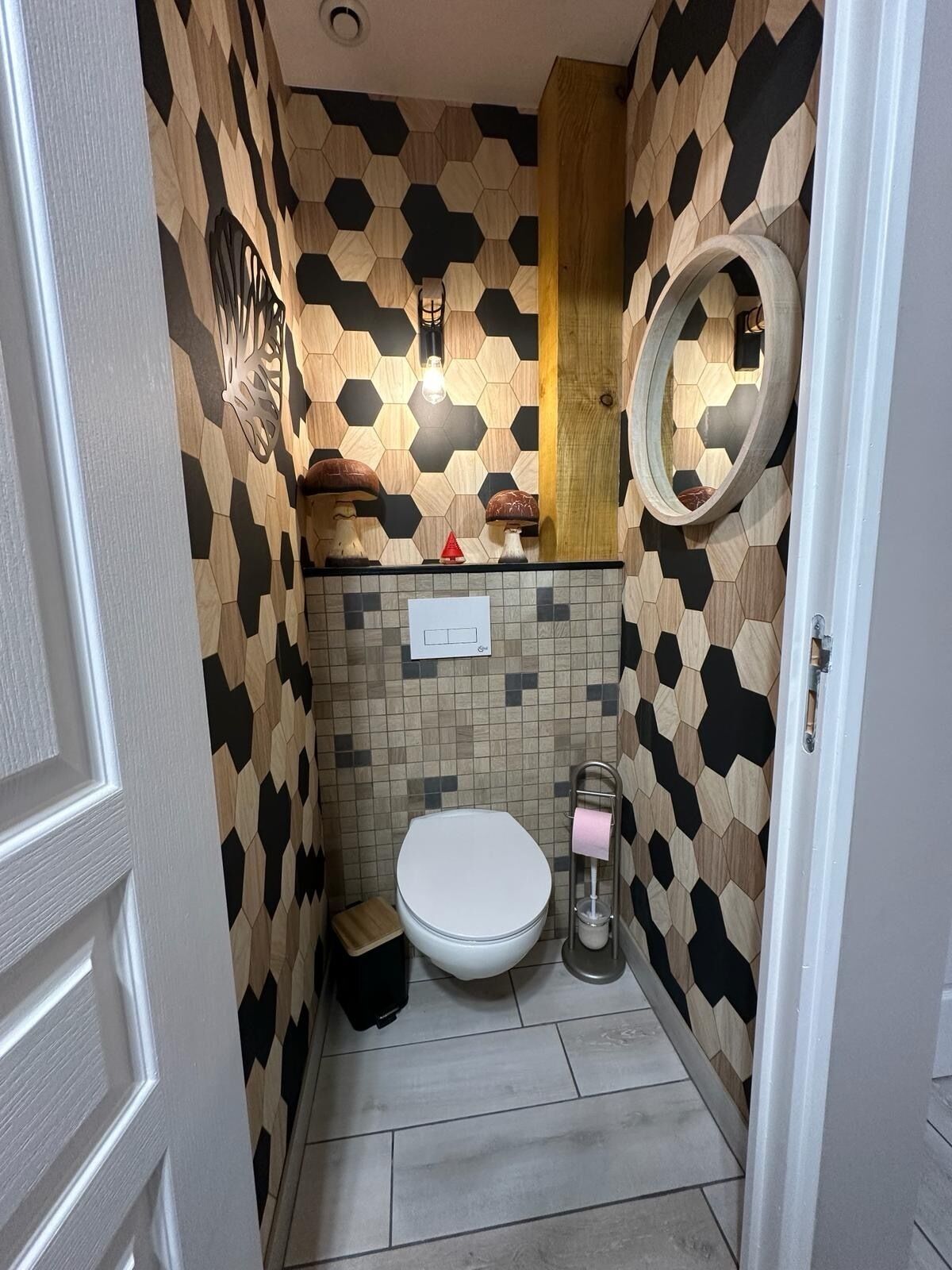 A small bathroom with a toilet, a sink, and a mirror. The walls are decorated with a geometric pattern.