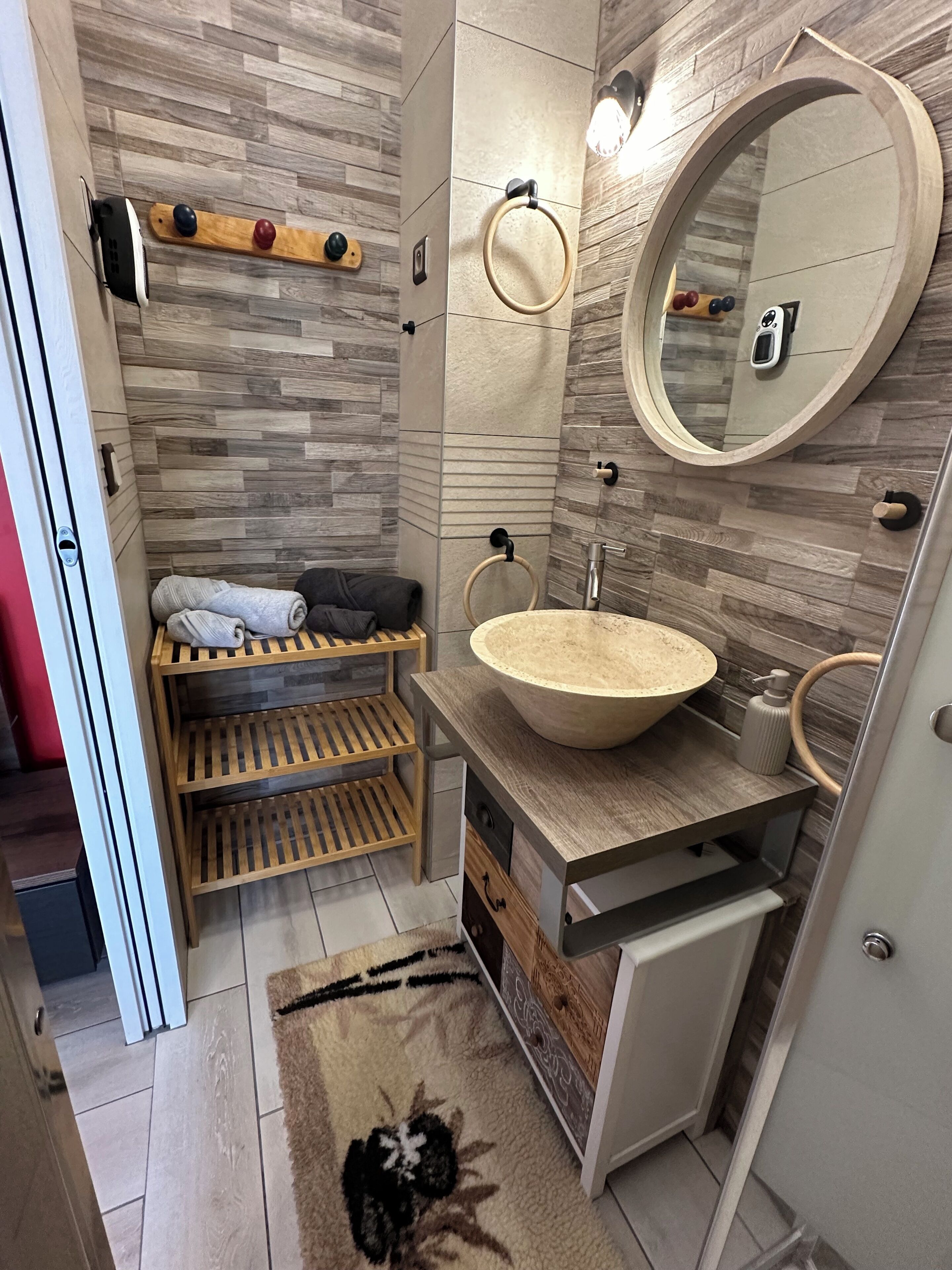 A modern bathroom with a wooden vanity, a round sink, and a large mirror.