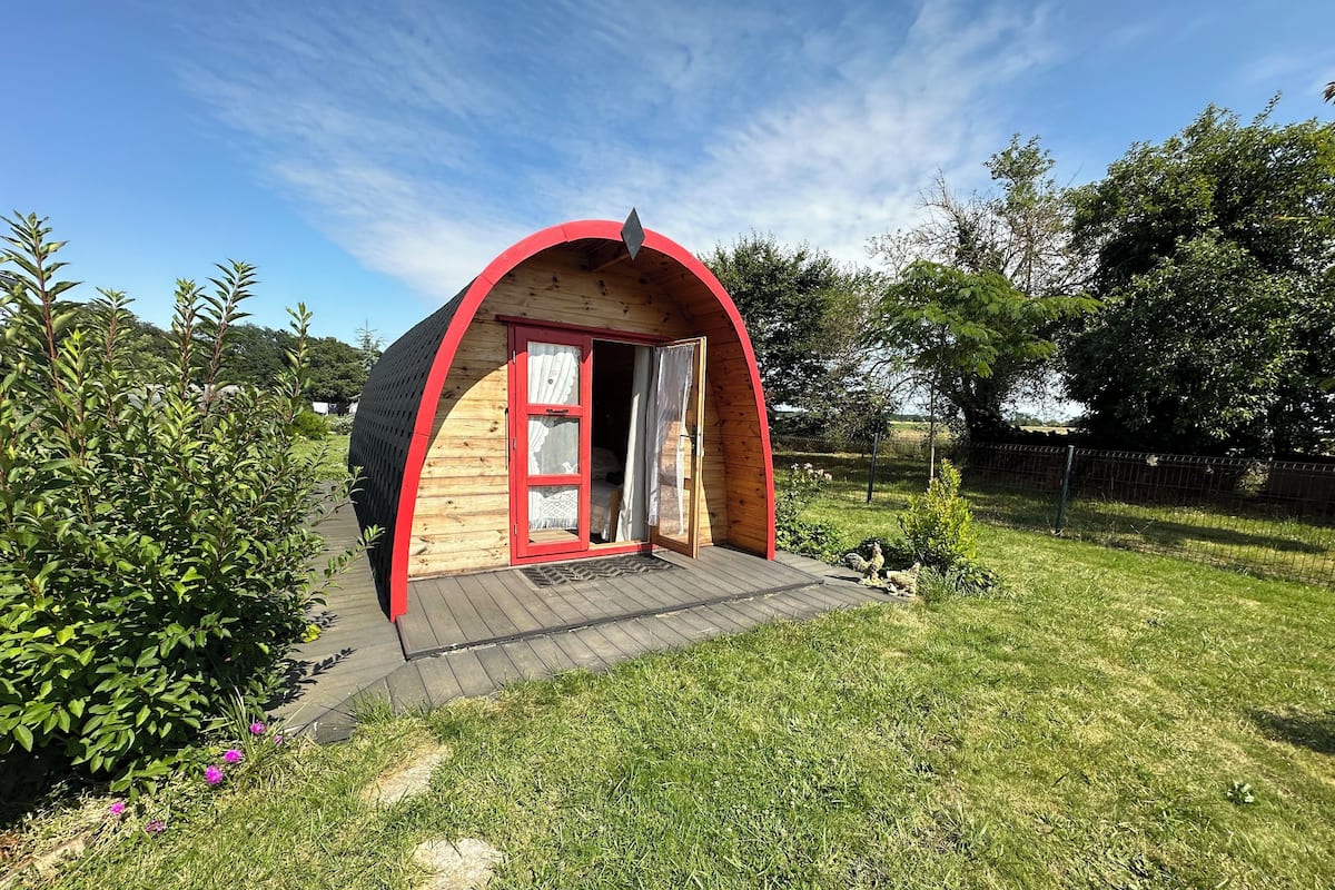 A small, semi-circular wooden structure with a red door and a wooden platform leading to it.