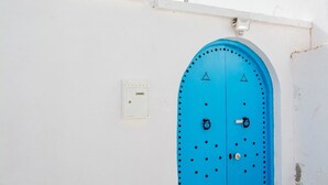 Una puerta azul junto a una pared blanca y un pequeño cuadro eléctrico.
