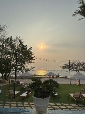 Relax on the beach with lounge chairs and umbrellas, surrounded by lush greenery and the soothing sound of the ocean.