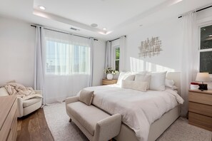 Ein modernes Schlafzimmer mit einem großen Bett, einem Nachttisch, einem Sessel und einem dekorativen Wandbild.