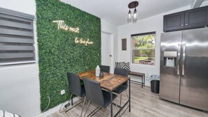 Cozinha moderna com parede verde, geladeira de aço inoxidável e área de refeições com mesa e cadeiras de madeira.