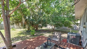 Quintal com deck de madeira, uma mesa e cadeiras, e um aparelho de ar condicionado grande.