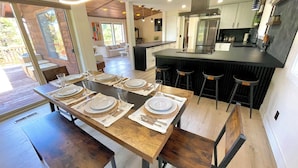 Een moderne keuken met een centraal eiland, barkrukken en een eethoek voor zes personen.