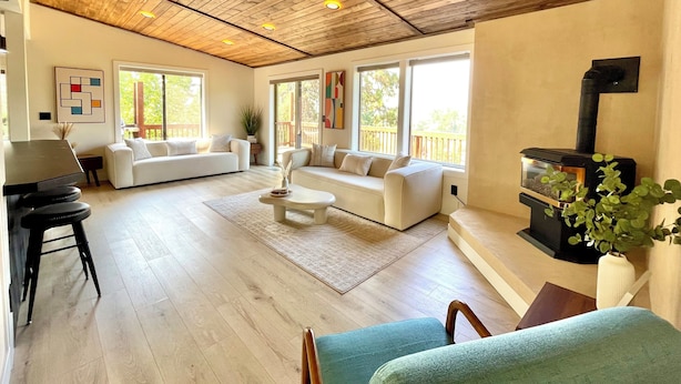 Een ruime woonkamer met houten plafond, grote ramen, een open haard en een zithoek.