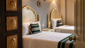 A hotel room with two beds, a wooden wardrobe, wall-mounted lights, and decorative sun motifs.