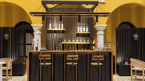 A bar area with a wooden counter, three stools, and shelves with bottles.